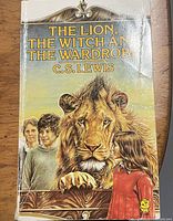 Cover photo of 'The Lion, The Witch and The Wardrobe' by C.S. Lewis, showing illustrations of a lion and children. Book is paperback with visible crease marks and edge wear.
