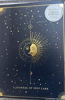 Cover of 'A Journal of Self Care' guided journal with dark blue cover and gold star and moon design