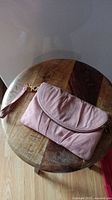 Pink clutch bag folded closed on wooden surface showing front side and wrist strap.