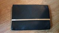 Closed purse showing black textured material with silver metal bar across front flap.