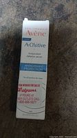 Photo of white and blue Avene A-Oxitive antioxidant defense serum outer box laying on a dark surface, text visible on front and side panels.