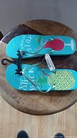 Top view of turquoise blue flip flops with pineapple and cocktail glass design and attached store tags and holder.