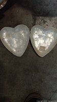 Two small heart-shaped plates with smooth, pearlescent surfaces shown from above.