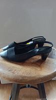 Side view of brand new women's black slingback shoe with modest heel on wooden stool.