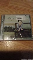 Front view of Enya music CD jewel case showing a seated woman on a bench artwork and a price sticker on the plastic wrap.