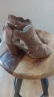 Side view of one light brown Fergalicious shoe on wooden stool, showing perforated pattern, block heel and peep toe.