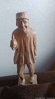 Front view of hand carved wooden statue of a man holding an object.
