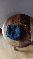 Photo of the blue beaded purse with chain strap lying flat on a round wooden stool.
