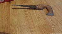 Hand saw with wooden handle laying on wood floor