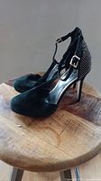 Black high heels shown from a side angle highlighting the ankle strap and studded heel