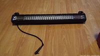 LED light bar approximately 22 inches long on wooden floor, showing black casing and cable for power connection