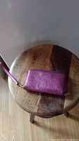 Closed view of hot pink Michael Kors wallet on wooden stool.