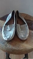 Front view of the silver metallic leather loafers showing moccasin-style toe stitching and slip-on design.