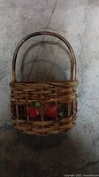 Top view of old wicker basket with handle and artificial apples inside, showing aged natural material and fruit decoration.