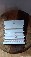 Photo of front side of set showing four pink-themed chokers with rhinestones, charms, and floral decorations on a white card.