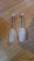 Photo showing two used shoe inserts with wooden handles and translucent plastic molds placed on a wooden floor.