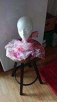 Photo showing pink silk scarf with flower patterns draped on a white mannequin head on a wooden stool.