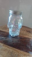 Side view of the clear glass skeleton-shaped mason jar placed on a wooden table, showing the skull details and silver lid