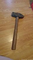 Photo of a 4 pound sledgehammer with a 12 inch wooden handle on a wood floor. The metal head is worn and the wooden handle is straight with a natural finish.