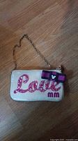 Front of small white bag showing decorative sequined pink text 'Love', purple and black bow with Mickey Mouse silhouette, and 'mm' letters at bottom right, gold chain strap visible