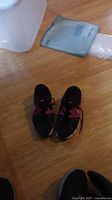 Photo of one pair of used women's Nike shoes on wooden floor with some background items