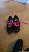 Photo of women's Nike shoes size 5.5 in black with vibrant pink laces placed on wooden floor.