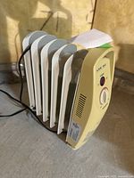 Side view showing five metal fins, control panel with temperature knob, red power indicator light, and power cord.