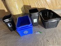 View of various bins on a carpeted floor showing a blue recycle bin, three black slim Type A bins, one large black Knobhill Farm bin, and two Sterilite bins with handles.
