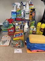 Lot of assorted cleaning supplies, spray bottles, boxes, powders, cloths, and sponges displayed on a table.