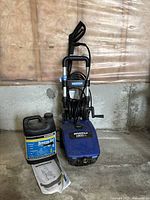 Full view of blue Simoniz electric pressure washer with attached spray gun, coiled hose, instruction manual, and washer fluid container.