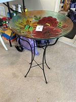 Full view of assembled bird bath showing colorful floral glass bowl mounted on black metal stand.