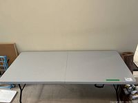 Full view of the gray folding plastic table in open position showing the plastic top and folding metal legs.