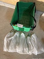 Photo showing five green plastic grocery boxes stacked with visible handles and five white mesh drawstring bags laid out in front.