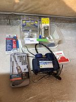 Overview photo showing 12V air compressor, ratchet driver set, contact cement, screws, and other tools arranged on floor.