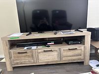 TV stand with flat-screen TV on top showing overall size and style. Three front compartments visible with the wood finish.