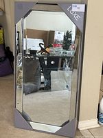 Front view of Luxe mirror standing against wall with corner packaging intact, showing size and beveled edge detail.