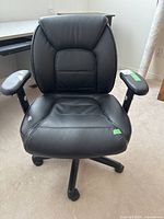 View of black office chair showing padded backrest and seat with damage to front left corner near edge.