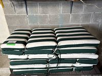 Stack of six green and white striped patio chair cushions tied on sides, shown in garage on concrete shelf.