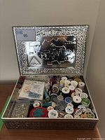 Overview of decorative metal box open showing assorted sewing items inside