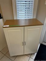 Front view of white storage cabinet with wood top and metal legs, doors closed.