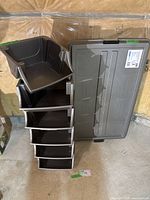 Stack of six black stackable storage bins with one grey lid, arranged to show bin shape and lid design.