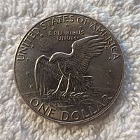 Photo of the obverse side of a 1978 Eisenhower One Dollar coin showing the eagle landing design, inscriptions, and minor surface wear.