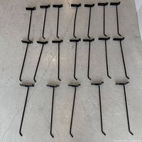 19 black commercial wall hooks laid out on concrete floor in rows, showing overall quantity and condition.