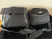 Two black carrying cases for portable DVD players placed side by side on a surface, showing strap details and flap closures.