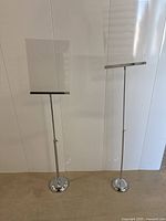 Photo showing two commercial display stands side by side, one shorter and one taller, each with clear acrylic sign holders and chrome round bases