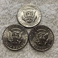 Three 1973 Kennedy half dollar coins showing the eagle seal on the reverse side, arranged in a triangular formation on a textured gray surface.