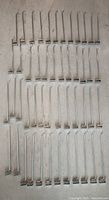 Full set of 48 identical chrome wall hooks laid out on a flat surface, showing the quantity and uniformity of the lot.