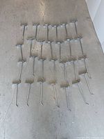 26 metal store hooks laid out flat on concrete floor showing length and angled design
