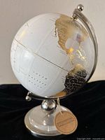 Front view showing the South Atlantic Ocean side of the globe with gold continents and white oceans, mounted on silver metallic stand.