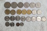 Photo showing 25 assorted international coins arranged on a white textured background, including silver-tone and gold-tone coins, different sizes and denominations.